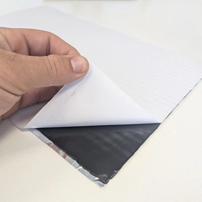 Hand peeling the white release paper from a self-adhesive sound deadening sheet