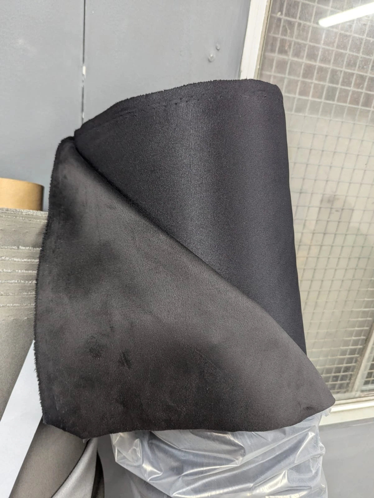 Actual dark suede lining fabric draped over the roll showing surface and reverse